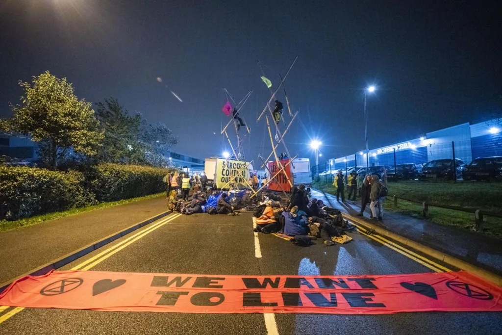 Protesters with banners and flags blockading a road at night to raise awareness for their cause.