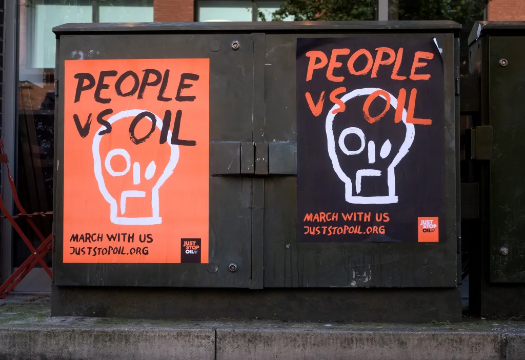 Two utility boxes with advocacy posters promoting environmental activism. the posters read "people vs oil", with a graphic design symbolizing a standoff between humanity and oil, inviting passersby to join a march for the cause.