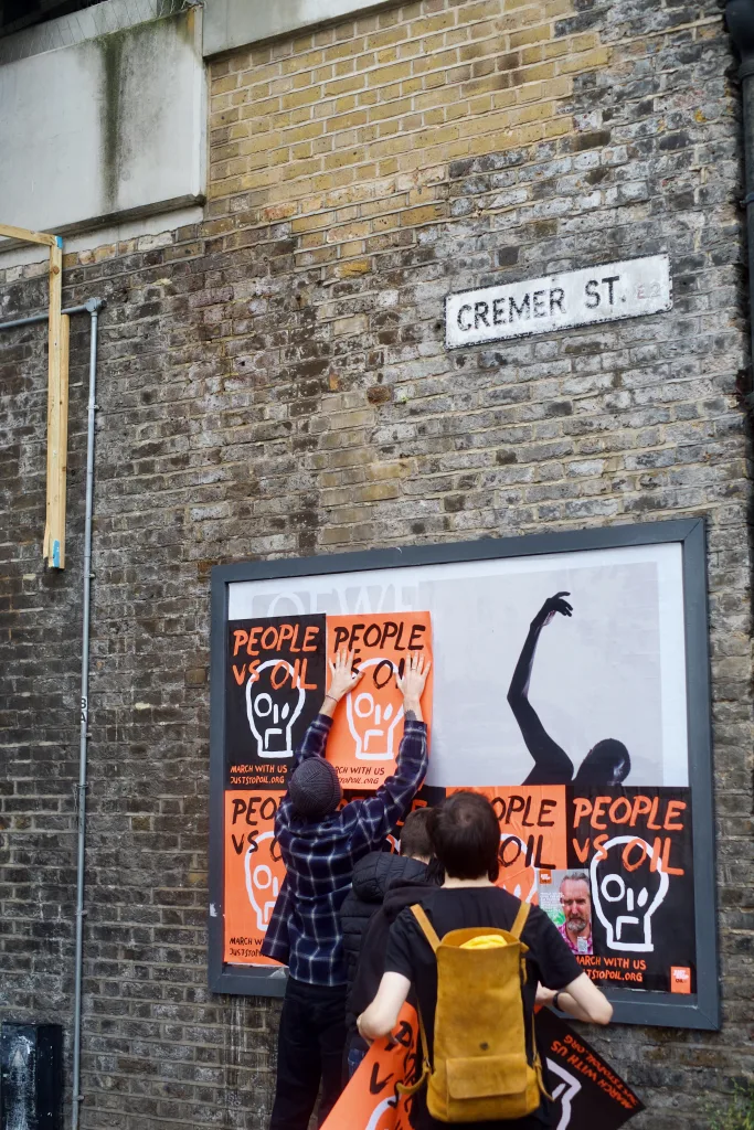 Two individuals standing by a wall with artistic posters, one of whom is reaching out to touch the artwork, on a street named cremer st.