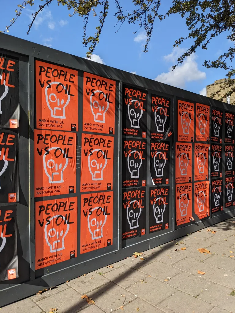 A row of vibrant orange and black protest posters on a public display board, promoting unity and action with the word "people" prominently featured and a graphic of a raised fist incorporated into a skull design.