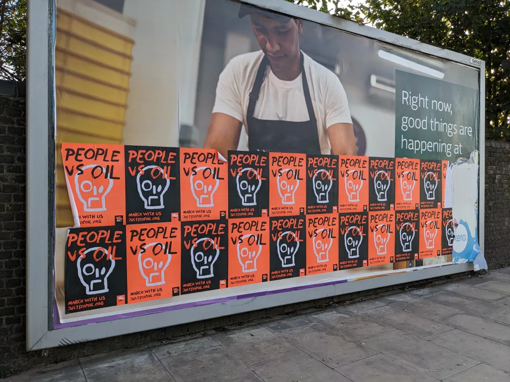 Billboard showing an advertisement with multiple stickers obscuring the main message, featuring a person working, with text on the right that reads, "right now, good things are happening at [obscured].