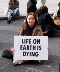 Young activist with a poignant message, sitting at a demonstration holding a sign that states "life on earth is dying".