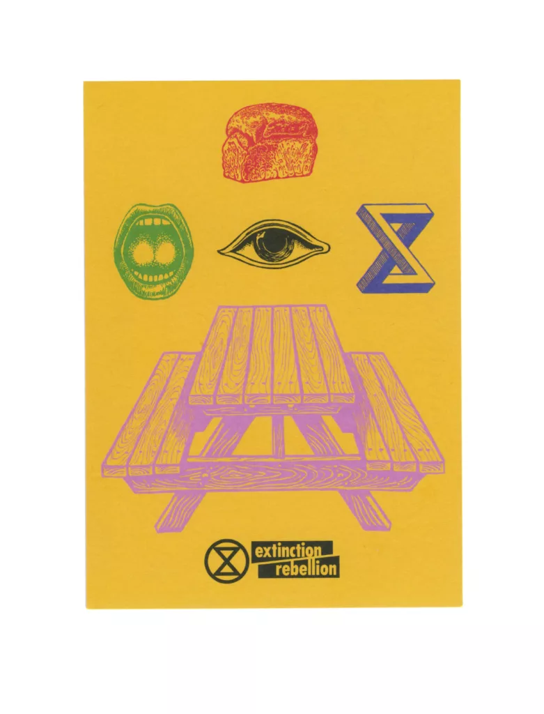 A vibrant graphic poster with a central illustration of a purple wooden picnic table on a yellow background, flanked by symbols – a red fist, a green hourglass inside a circle, a blue 'x', and an eye – representing various aspects of activism, with the "extinction rebellion" logo at the bottom.