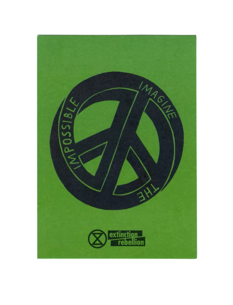 A green pamphlet with the extinction rebellion logo printed in black, featuring the words "impossible, imagine, the" in a circular arrangement around their symbol.