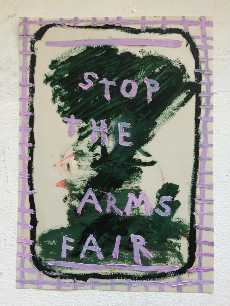 A painting of the cloud from a bomb includes pink words painted over the top that say stop the arms fair by daisy parris