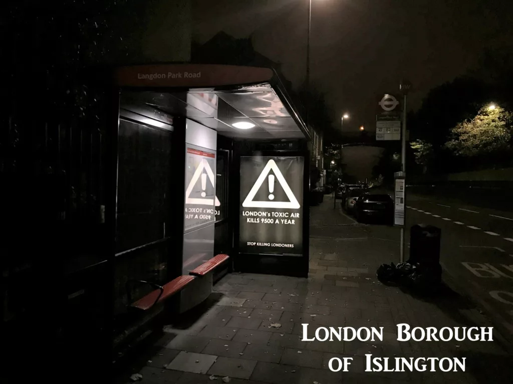 A bus stop advert lit up at night calls to reduce air pollution in London.