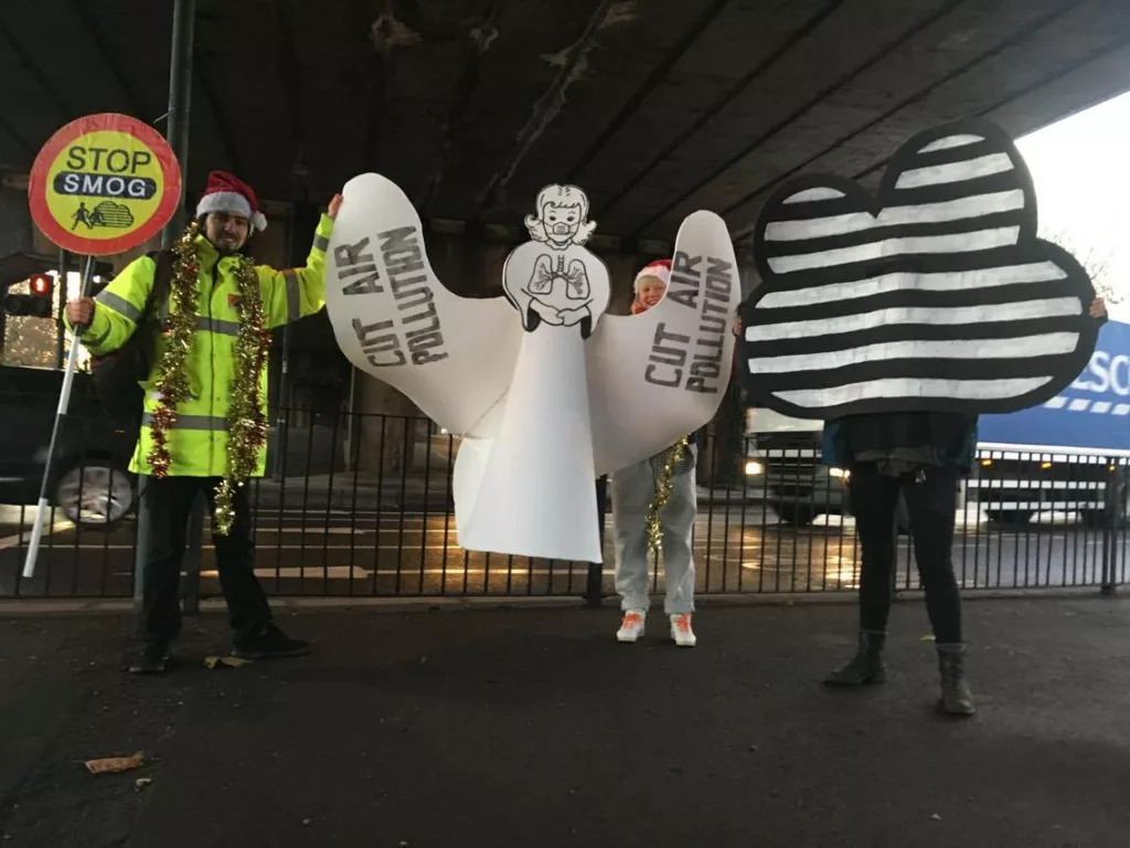 A person dressed as a lollypop lady stands withan angel and a smog cloud costume.