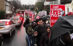 People march through a residential street with placards saying save lewisham A&E