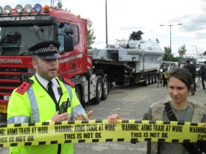 Someone blocks a vehicle carrying weapons to the arms fair as the police try to talk to them.