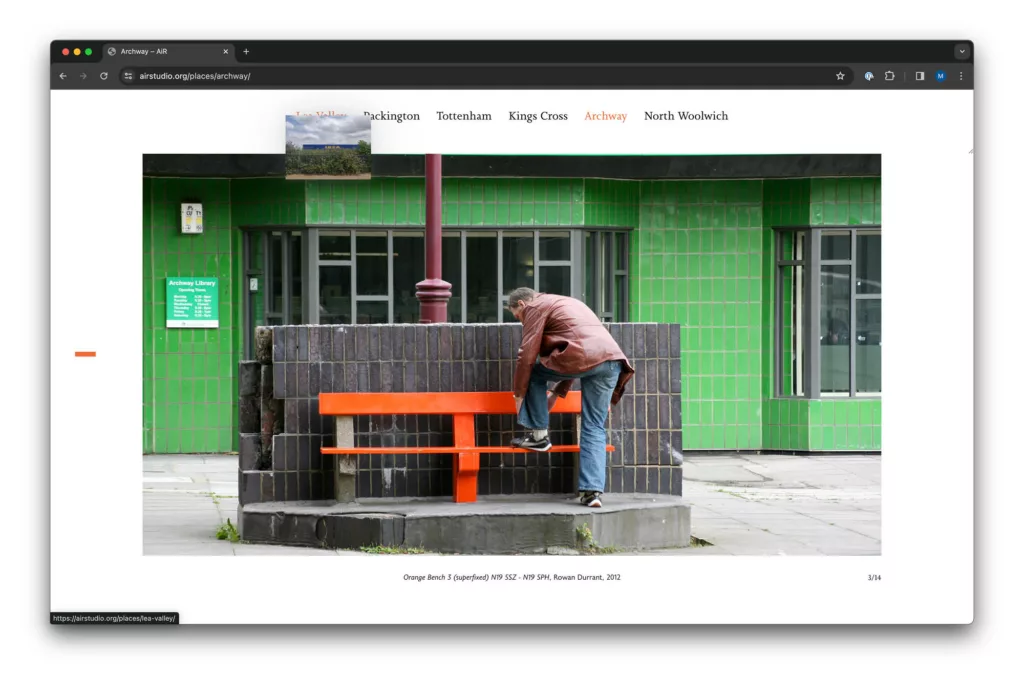 A person is leaning over a wooden railing painted in orange, looking at something on a green-tiled building's exterior, creating a vivid contrast of colors.