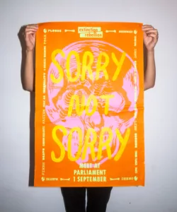 Person holding a vibrant protest poster for environmental action, with bold text 'sorry not sorry' emphasizing the urgency for meeting at parliament.