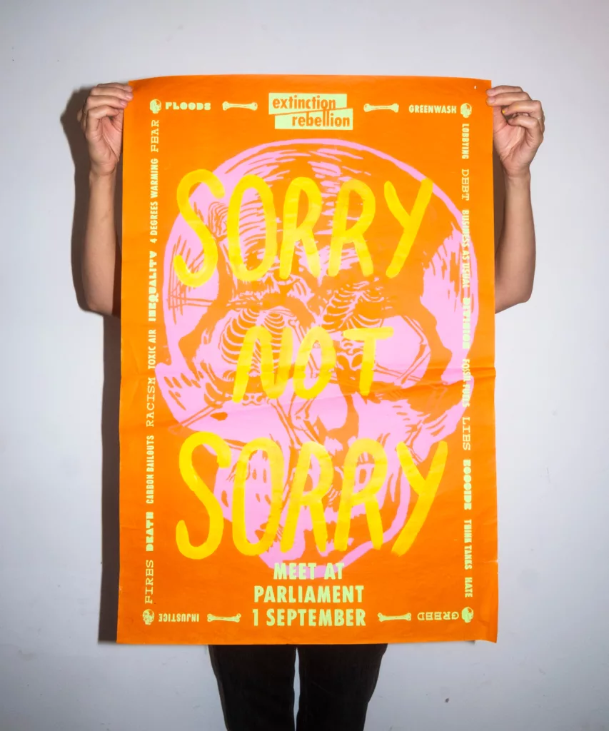 Person holding a vibrant protest poster for environmental action, with bold text 'sorry not sorry' emphasizing the urgency for meeting at parliament.