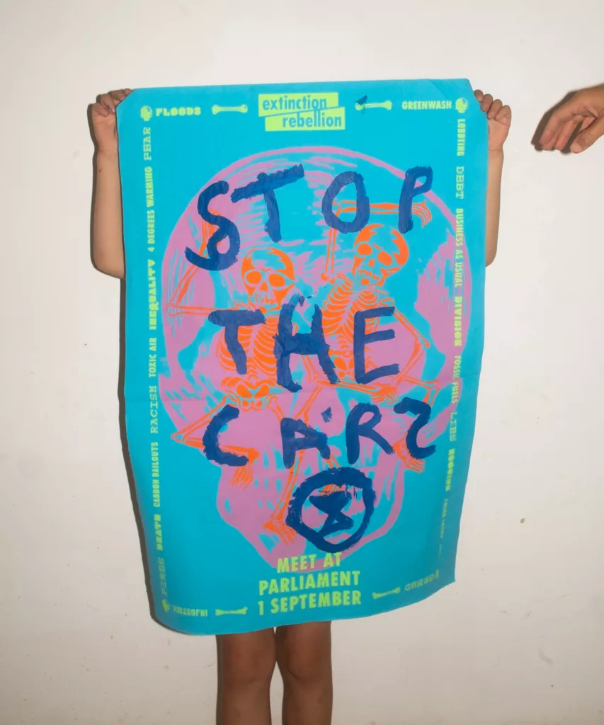 Activist holding up a brightly colored protest poster from extinction rebellion with a message to stop the destruction of the environment, signaling a rally at parliament on september 1st.