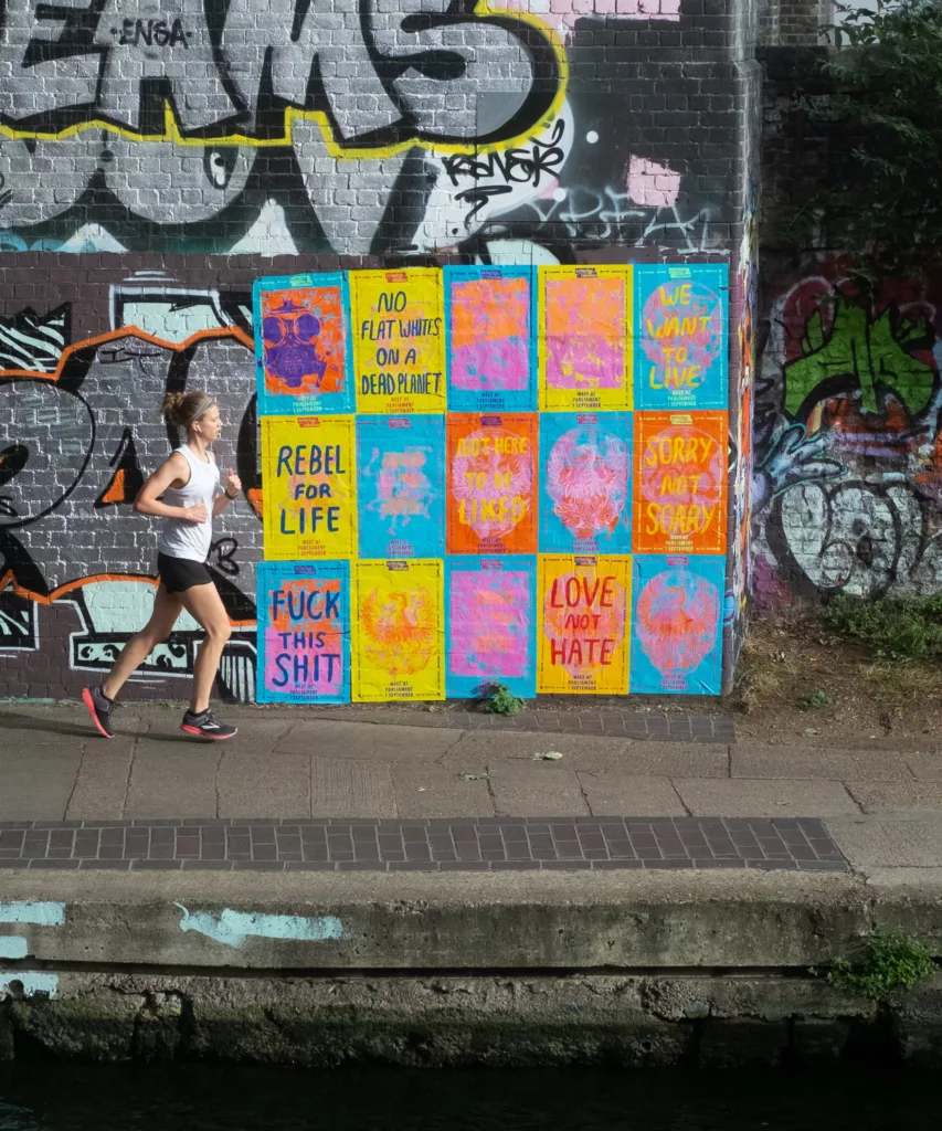 A runner in motion next to a colorful graffiti wall with various statements and vibrant patterns.