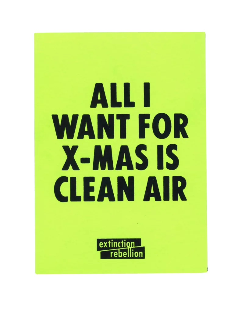 A bright neon sign with the message "all i want for x-mas is clean air" attributed to extinction rebellion, advocating for environmental awareness and action against pollution.