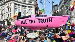 An activist stands on a pink boat that has a message on the side Tell The Truth in the middle of oxford circus